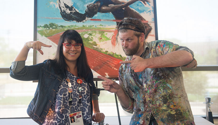 Carla Morris and Peter Farmer pose in front of the high jump painting at the Art of the Games live auction