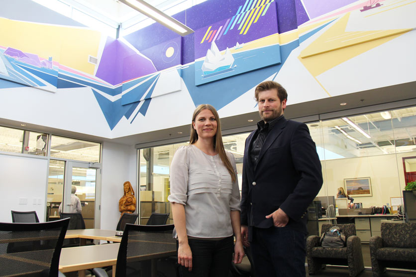 Peter Farmer (à droite) et Cherry Eidse, coordonnatrice des installations, CWB National Leasing, devant la murale de Peter dans la salle Canada, à CWB National Leasing.